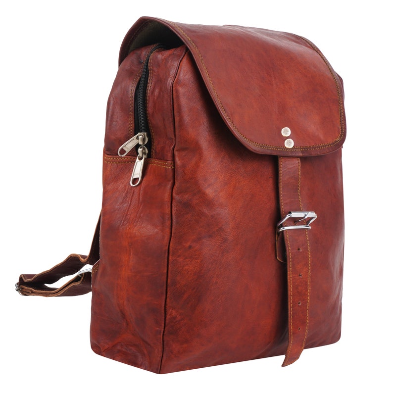 May include: A brown leather backpack with a flap closure and adjustable buckle. The backpack features a zippered front pocket and adjustable shoulder straps. The leather has a distressed appearance, and the hardware is silver-toned.