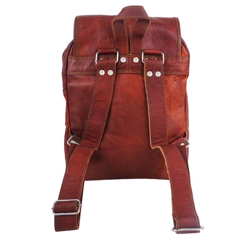 May include: A brown leather backpack with adjustable shoulder straps and a flap closure. The backpack features silver-colored metal hardware and visible stitching details. The bag is made of a rich, textured leather.