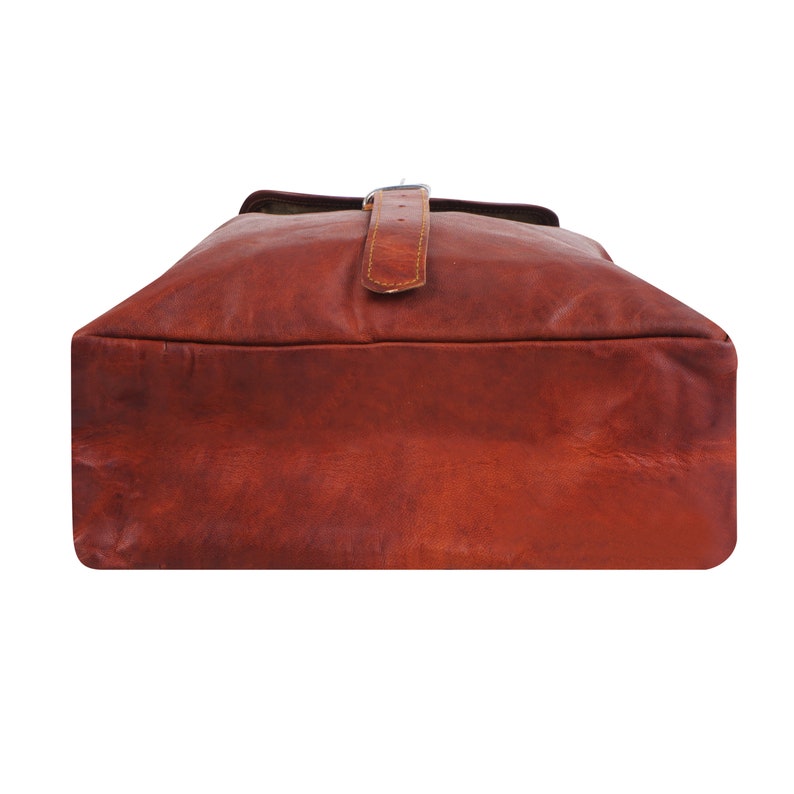 May include: A brown leather backpack with a rectangular shape. The bag has a flap closure secured by a leather strap and a metal buckle. The leather has a distressed appearance.