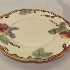 May include: Off-white ceramic plate with a scalloped edge and a brown rim. The plate is decorated with hand-painted red and yellow apples, green leaves, and brown branches.