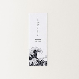May include: A white bookmark featuring a black and white illustration of a wave. The text "He calms the raging sea." and "PSALM 89:9" are printed in black. The bookmark has a minimalist design.