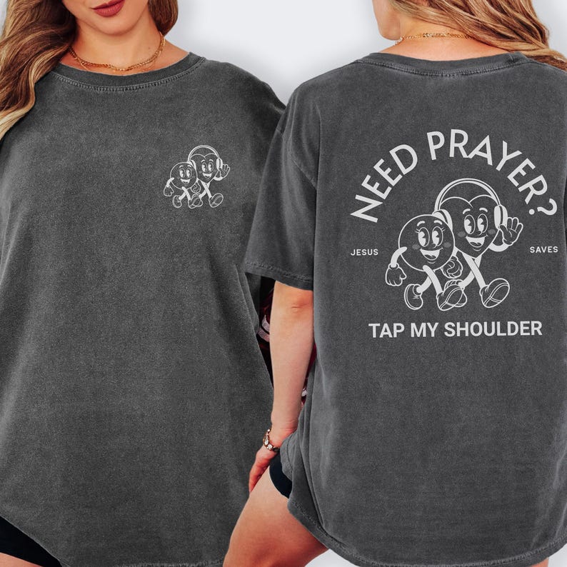 May include: Dark gray t-shirt with a graphic of two cartoon characters with headphones. The back of the shirt reads "Need Prayer? Tap My Shoulder" with the words "Jesus Saves".