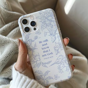 May include: White phone case with a floral design in light blue. The case features the text "Be still, and know that I am God. Psalm 46:10" and a small bird illustration. The case is designed for a smartphone.