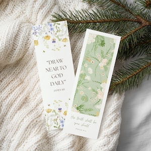 May include: Two rectangular bookmarks with floral designs and inspirational quotes. One bookmark features the text "DRAW NEAR TO GOD DAILY" and the other reads "His truth shall be your shield." The background is a white knit fabric.