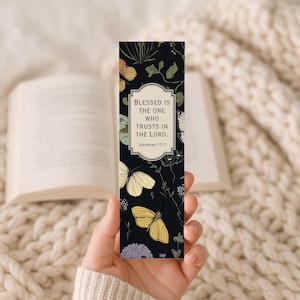 May include: A black bookmark featuring a floral and butterfly design. The bookmark has the text "Blessed is the one who trusts in the Lord. Jeremiah 17:7" in a white frame. The butterflies are yellow, orange, and white.