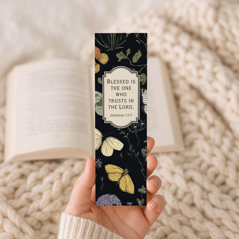 May include: A black bookmark featuring a floral and butterfly design. The bookmark has the text "Blessed is the one who trusts in the Lord. Jeremiah 17:7" in a white frame. The butterflies are yellow, orange, and white.