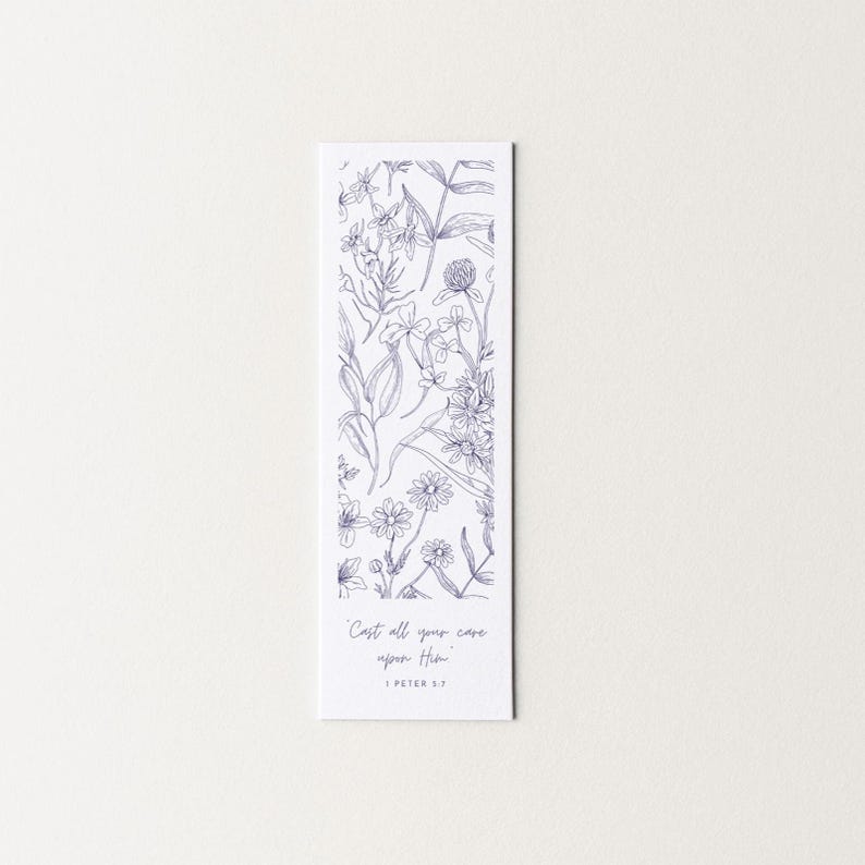 May include: A rectangular white bookmark with a detailed blue floral illustration. The design includes various flowers and foliage. The text "Cast all your care upon Him" and "1 Peter 5:7" are printed in a delicate script at the bottom.
