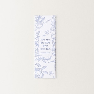 May include: A white bookmark with a blue floral design and the text "You are the God who sees me. Genesis 16:13". The bookmark features a bird and botanical illustrations.