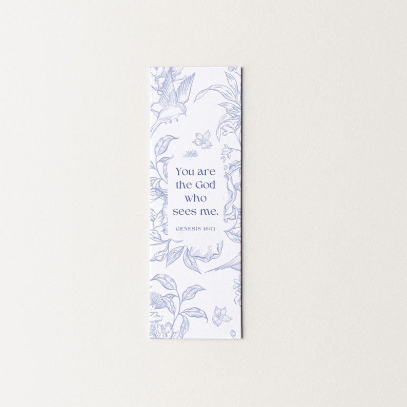 May include: A white bookmark with a blue floral design and the text "You are the God who sees me. Genesis 16:13". The bookmark features a bird and botanical illustrations.