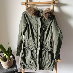 May include: A green hooded winter jacket with a faux fur trim around the hood. The jacket has a button closure, two large pockets, and a drawstring waist.