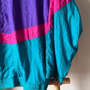 Pode incluir: Uma jaqueta corta-vento vintage com design de blocos de cores. A jaqueta &eacute; feita de tecido de nylon leve e apresenta um esquema de cores roxo, rosa e turquesa. A jaqueta tem fecho de correr e gola alta.