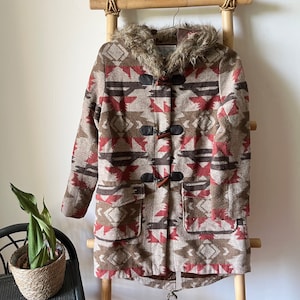 May include: A brown, red, and beige patterned fleece jacket with a faux fur hood and toggle closures. The jacket has a geometric pattern and is lined with a brown fabric.