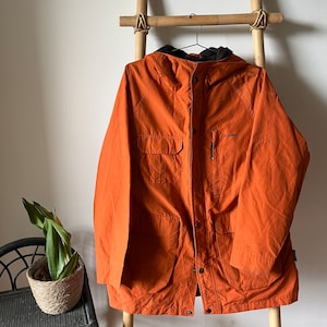 May include: A bright orange hooded jacket with a zip fastening and multiple pockets. The jacket has a black logo that says "Gerry" on the left chest.