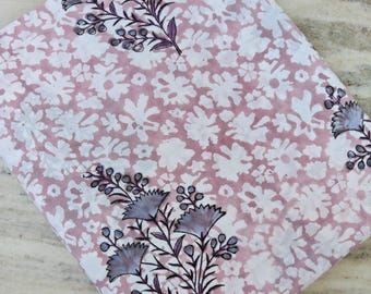 May include: A folded fabric with a floral pattern. The fabric has a light pink background with white floral shapes. Dark purple floral branches with light blue flowers are printed on the fabric.