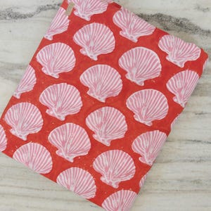 Pode incluir: Tecido vermelho com um padrão repetido de desenhos de conchas rosa e brancas. As conchas têm linhas detalhadas, criando uma aparência texturizada. O tecido está dobrado, mostrando a continuidade do padrão.