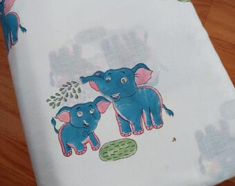 Puede incluir: Tela blanca con un patrón repetido de elefantes azules con orejas y detalles rosas. Los elefantes están representados en un estilo de dibujos animados, con una expresión amigable. También hay formas verdes en forma de hojas.