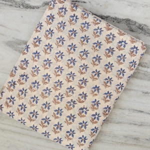 Könnte beinhalten: Gefalteter Stoff mit einem sich wiederholenden Blumenmuster. Die Blumen sind blau mit braunen Stielen und Blättern, vor einem cremefarbenen Hintergrund. Der Stoff ist wahrscheinlich Baumwolle oder ein ähnliches Material, geeignet für Näh- oder Bastelprojekte.