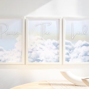 Puede incluir: Tres impresiones artísticas enmarcadas con las palabras "Praise The Lord" en escritura elegante. Cada impresión presenta una escena de cielo con nubes blancas esponjosas sobre un fondo azul claro y amarillo. Los marcos son blancos.