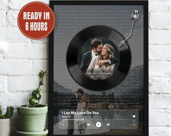 May include: A framed black and white photo of a wedding couple with a black vinyl record in the background. The record has the couple's names and wedding date, "Katherine & Christopher, March 15, 2023." The record is playing the song "I Lay My Love On You" by Westlife.