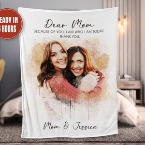 K&ouml;nnte beinhalten: Eine wei&szlig;e Fleece-Decke mit einem Aquarell-Bild von zwei Frauen, die sich umarmen. Der Text "Dear Mom" befindet sich oben auf der Decke, gefolgt von "Because of you, I am who I am today. Thank you." Der Text "Mom & Jessica" befindet sich unten auf der Decke.
