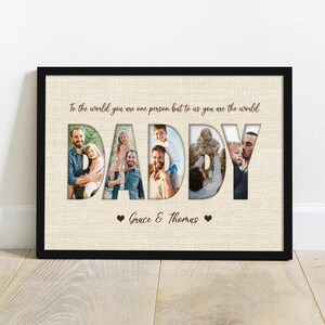 May include: A framed print with the word "DADDY" cut out to reveal family photos. The print has a beige background with the text "To the world you are one person but to us you are the world" and the names "Grace & Thomas".