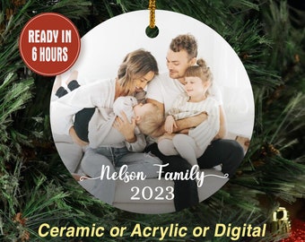 May include: A round Christmas ornament with a family photo, the text "Nelson Family 2023", and the words "Ceramic or Acrylic or Digital". The ornament has a gold string for hanging and the text "READY IN 6 HOURS" in a red circle.