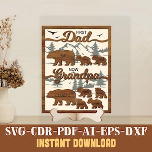 May include: Wooden framed sign with the words "First Dad Now Grandpa" and bear family silhouettes. The sign includes names of family members. The sign is displayed on a white stand.