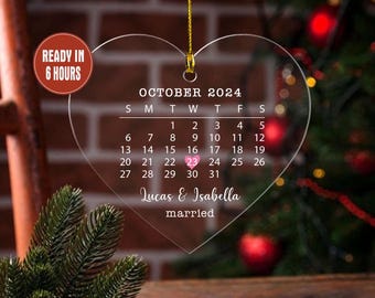 May include: Clear heart-shaped ornament with a gold string, featuring a calendar for October 2024. The date October 23rd is highlighted. The names "Lucas & Isabella" and the word "married" are also displayed.