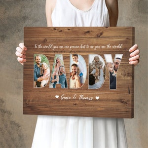 May include: Wooden canvas art with the word "DADDY" in large, white letters. The letters are filled with family photos. The text "To the world you are one person but to us you are the world" is above the word "DADDY". The names "Grace & Thomas" are below.