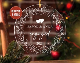 Könnte beinhalten: Transparenter Verlobungsschmuck aus Acryl mit goldenem Aufhänger. Der Schmuck hat ein weißes Blumengirlanden-Design, zwei Herzen und die Namen "JASON & ANNA", mit dem Wort "engaged" und dem Jahr "2024". Ein roter Kreis liest "READY IN 6 HOURS".
