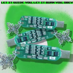 以下が含まれることがあります： 銀色の蝶のチャームが付いた緑色の回路基板が3枚。回路基板には「P+ 11.30V」、「B2+ 7.4V」、「VOL」、「R010」、「P+ 11.10V」、「B2+ 7.4V」、「R010」、「B1+ 3.7V」の文字が書かれている。