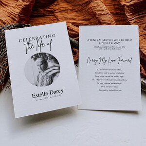 以下が含まれることがあります： 2 つの白い追悼カード。左側のカードには、白黒写真とともに「Estelle Darcyの人生を祝う」と書かれています。右側のカードには「2029年7月23日に葬儀が行われます」と「Carry My Love Forward」と書かれています。