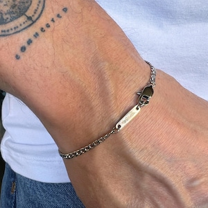 Könnte beinhalten: Ein silbernes Kettenarmband mit einem kleinen silbernen Anhänger, auf dem "LOVE" steht.
