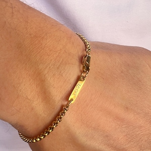 Peut inclure: Un bracelet doré avec un motif de chaîne en forme de boîte. Le bracelet comporte un charm rectangulaire avec le mot "LOVE" gravé. Le bracelet est sécurisé par un fermoir mousqueton.