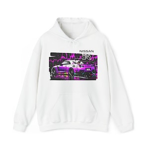 Puede incluir: Sudadera blanca con un gráfico de un coche Nissan GT-R morado en la parte delantera. El coche está rodeado de salpicaduras de pintura rosa y blanca. El texto "NISSAN GT-R" está impreso sobre el coche.