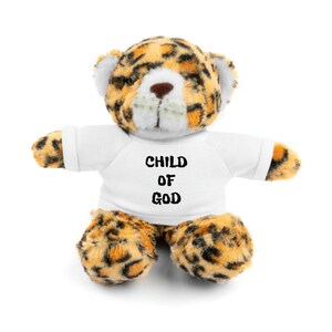 Puede incluir: Un oso de peluche de estampado de leopardo con una camiseta blanca con el texto "CHILD OF GOD" impreso.