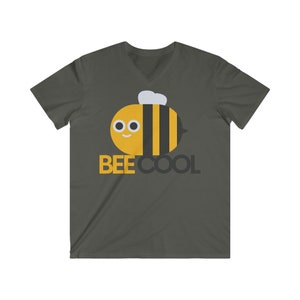 Puede incluir: Una camiseta de cuello en V gris oscuro con un gráfico de abeja de dibujos animados y el texto "BEE COOL" en letras negras.