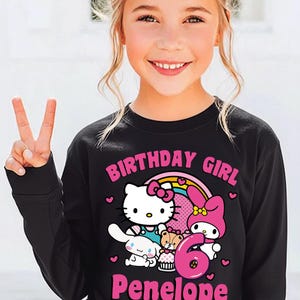 May include: Black long-sleeve shirt featuring a colorful graphic of Hello Kitty, My Melody, and other characters, with the text "BIRTHDAY GIRL", the number "6", and the name "Penelope".