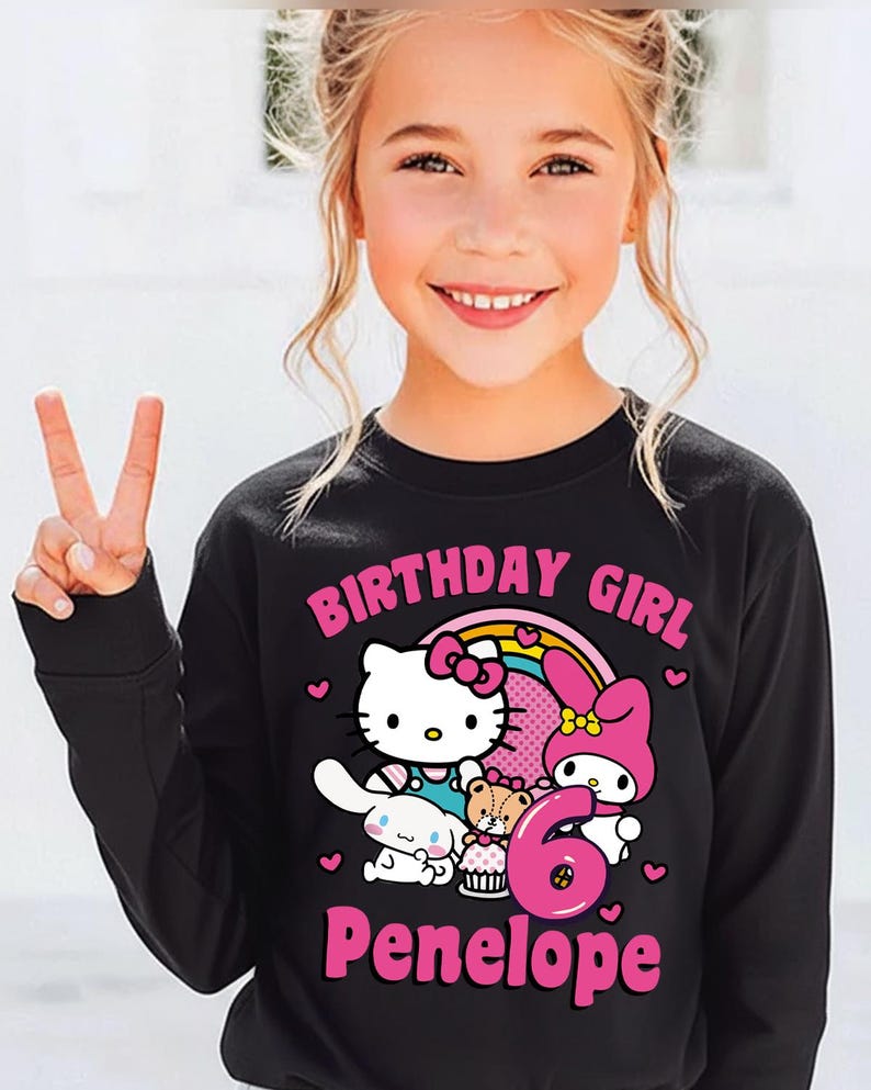 May include: Black long-sleeve shirt featuring a colorful graphic of Hello Kitty, My Melody, and other characters, with the text "BIRTHDAY GIRL", the number "6", and the name "Penelope".
