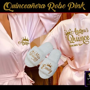 Peut inclure: Robe en satin rose avec broderie dorée disant "Andrea's Quince 10.01.2022" au dos. La robe a une ceinture assortie et est livrée avec deux pantoufles blanches avec broderie dorée disant "Mis Quince" et "Emily".