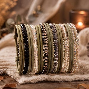 Könnte beinhalten: Ein mehrsträngiges Armband mit olivgrünen Kordelbändern, die mit Reihen facettierter Perlen in Schwarz, Transparent, Bronze und Champagner durchsetzt sind. Das Design besteht aus mehreren parallelen Strängen, die durch olivgrüne Kordelknoten gehalten werden.