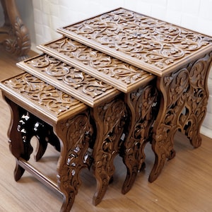May include: Set of three nesting tables made of dark brown wood. Each table features intricate floral carvings on the tabletop and legs. The tables are arranged in a nested configuration, with the smallest table tucked under the larger ones.