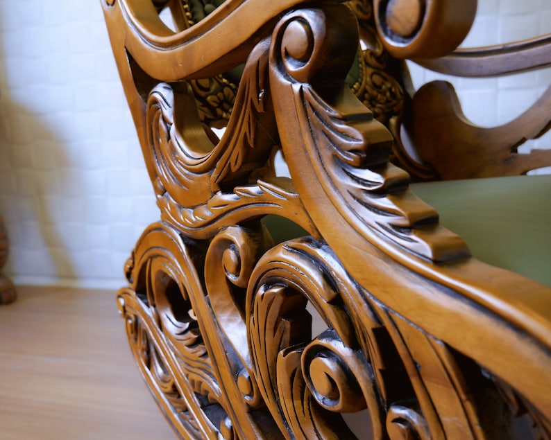 May include: Close-up of a wooden rocking chair with intricate carvings. The chair is made of dark wood with a natural finish. The carvings are detailed and ornate, featuring floral and scroll designs.