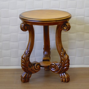 May include: A round wooden side table with intricate carvings on the legs and a smooth, brown top.