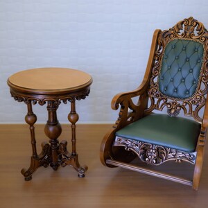 May include: A wooden table with a round top and three legs, and a carved wooden rocking chair with a green upholstered seat.
