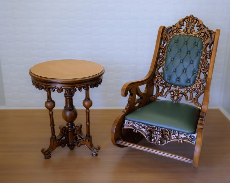 May include: A wooden table with a round top and three legs, and a carved wooden rocking chair with a green upholstered seat.