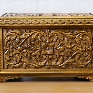 Peut inclure: Une boîte en bois avec des motifs floraux sculptés complexes. La boîte est de couleur brun foncé et a un couvercle à charnières.