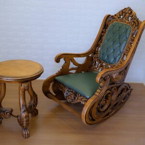 May include: A wooden rocking chair with intricate carvings and a green upholstered seat. A small wooden table with a round top sits next to the chair.