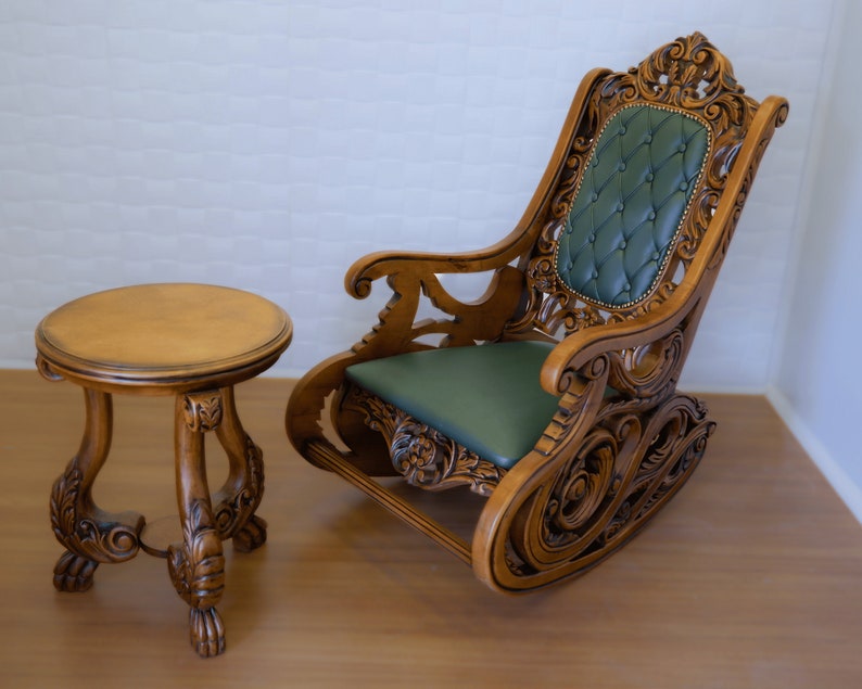 May include: A wooden rocking chair with intricate carvings and a green upholstered seat. A small wooden table with a round top sits next to the chair.