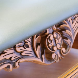 May include: A wooden table with a light green top and intricate carved details around the edge. The carving features a floral design with a central motif of three rounded shapes.
